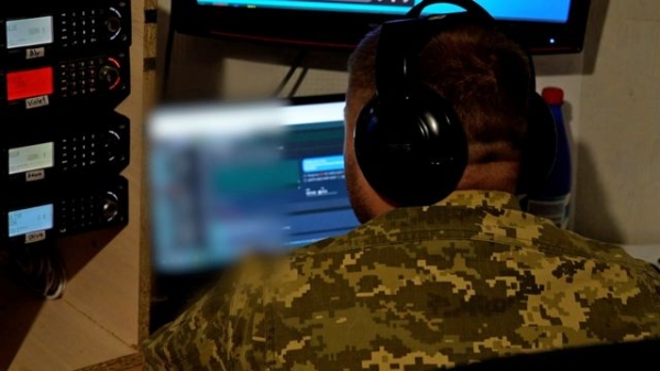 Ukrainian soldier leans over his laptop in a damp basement